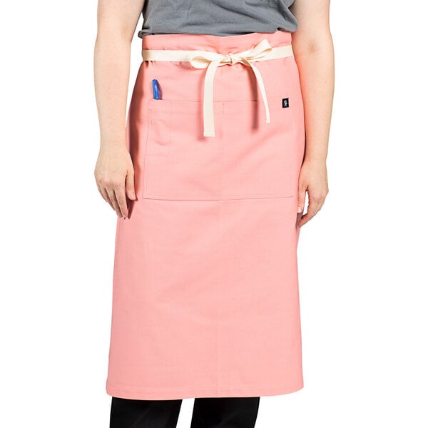 A woman wearing a coral pink Uncommon Chef bistro apron with a pocket.
