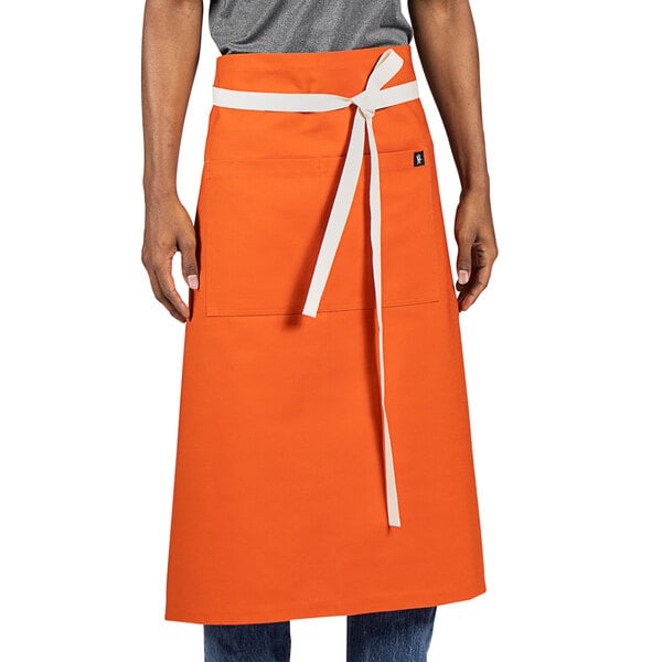 An orange Uncommon Chef bistro apron with a white belt on a counter.