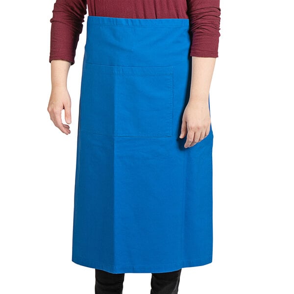 A woman wearing a blue Uncommon Chef bistro apron with black webbing standing in a professional kitchen.