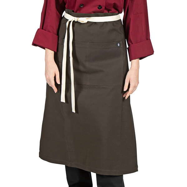 A woman wearing a dark brown Uncommon Chef bistro apron with natural webbing.