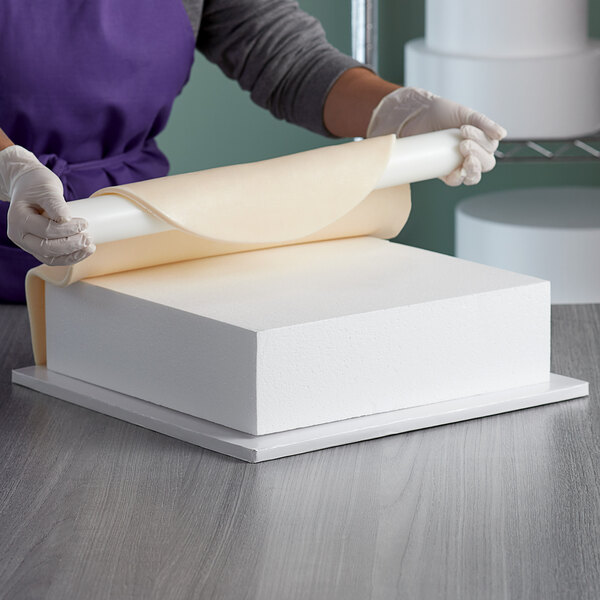 A woman using a Baker's Mark foam square cake dummy to roll out dough.