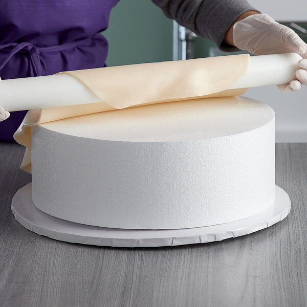 A person rolling a Baker's Mark foam round cake dummy on a table.