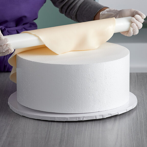 A person wrapping a Baker's Mark foam round cake dummy with paper.
