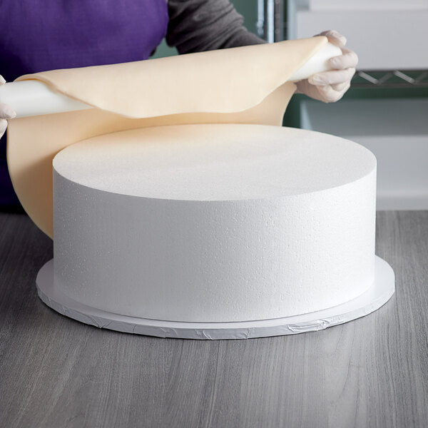 A person wrapping a foam cake dummy with a roll of paper.