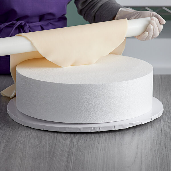 A person holding a Baker's Mark foam round cake dummy on a table.