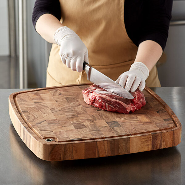 A person cutting meat on a Fox Run acacia wood chopping block.