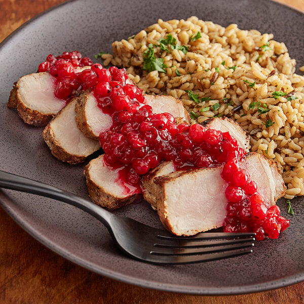 A plate of meat and rice with red currant sauce on a table with a fork.