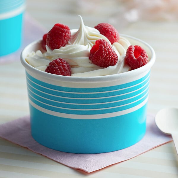 A blue paper Choice food cup filled with ice cream topped with raspberries.