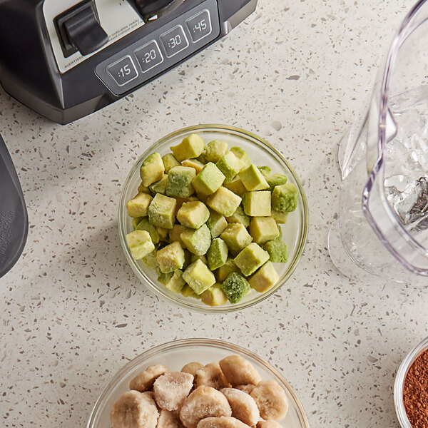 A bowl of diced avocados next to a blender with food in it.
