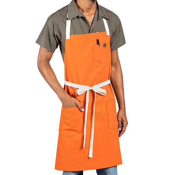 A person wearing an orange Uncommon Chef bib apron with natural webbing and pockets.