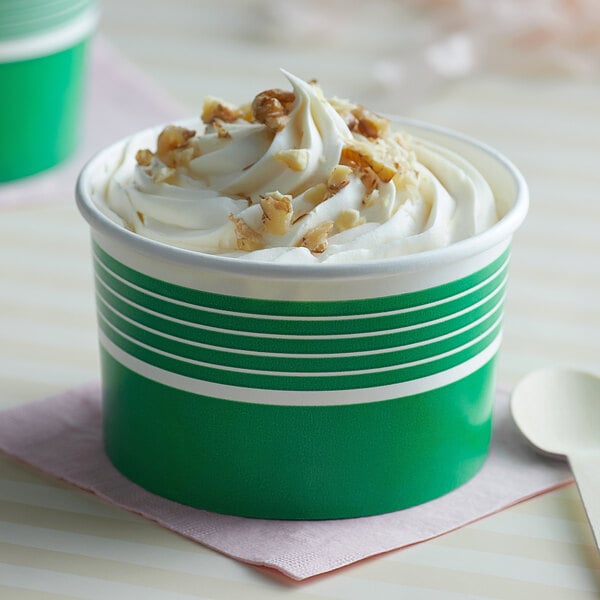 A close up of two green Choice paper cups filled with ice cream, whipped cream, and nuts.