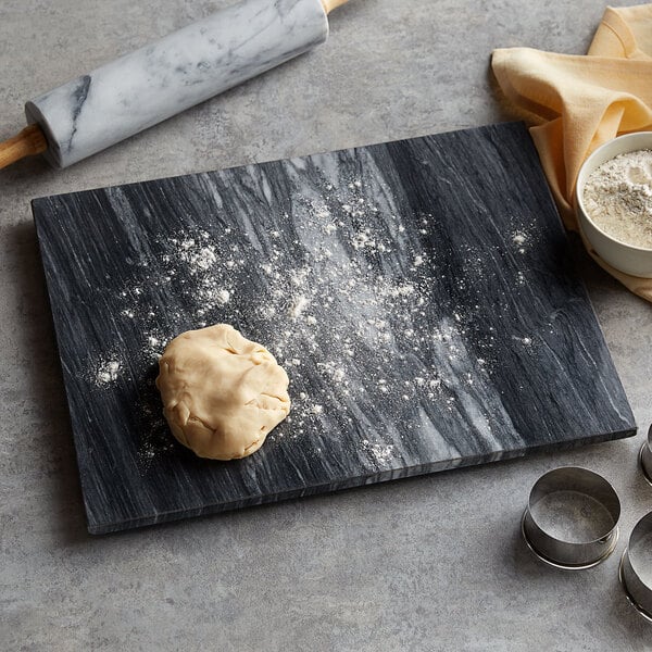 A ball of dough on a black and white marble pastry board next to a rolling pin.