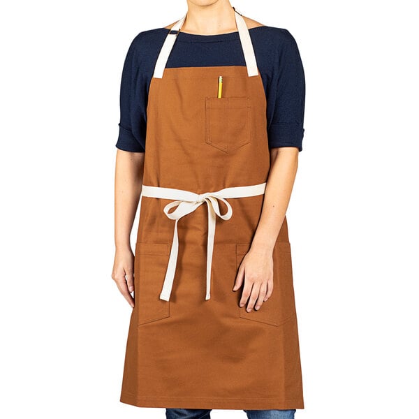 A woman wearing a customizable Uncommon Chef canvas bib apron with pockets.