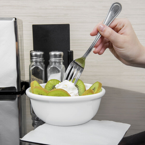 A hand holding a fork over a bowl of kiwi and whipped cream.