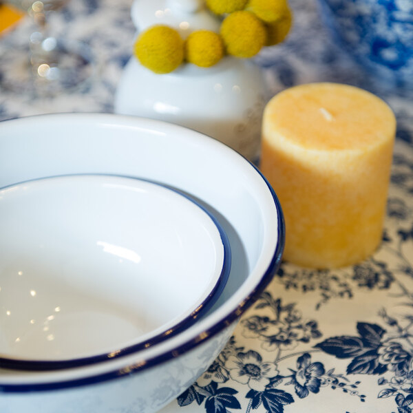 A close-up of a Crow Canyon Home white enamelware footed bowl with a blue rim on a table.