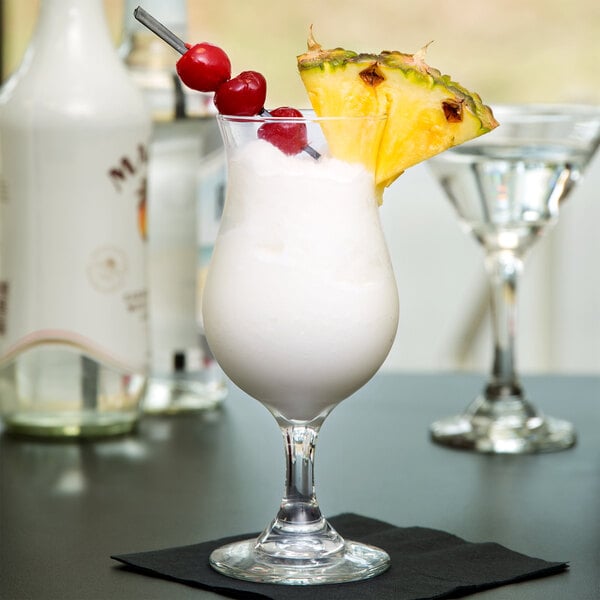 A Libbey Poco Grande glass filled with a white drink and garnished with pineapple and a cherry.
