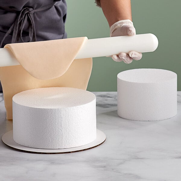 A person holding a Baker's Mark white foam cylinder over several rolls of paper.