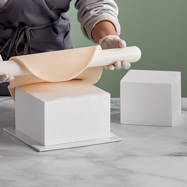 A person rolling out a cake dummy with a rolling pin.