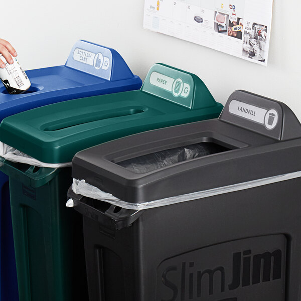 A woman using a Rubbermaid Waste Stream Label Kit to label a green and blue trash can for recycling.