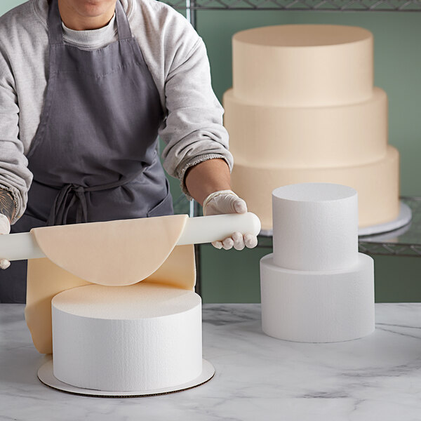 A woman using a rolling pin to make a cake on a white surface.
