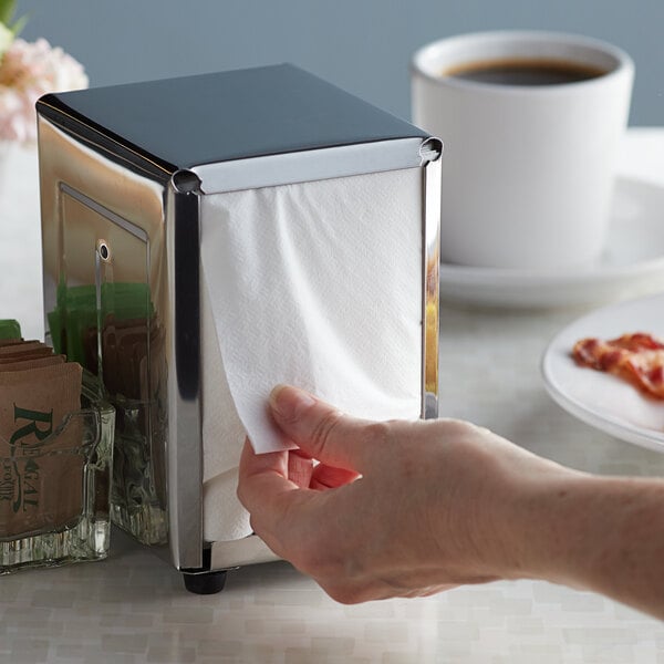A hand pulling a Choice White Junior Low-Fold napkin out of a dispenser on a counter.
