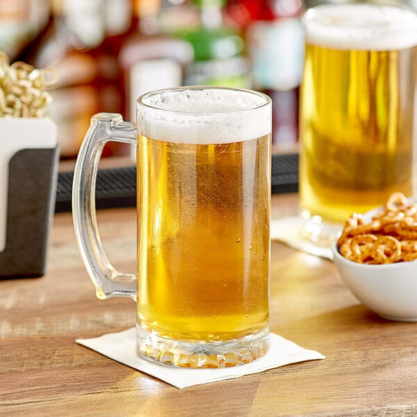 Two Acopa beer mugs filled with beer on a table with a bowl of pretzels.