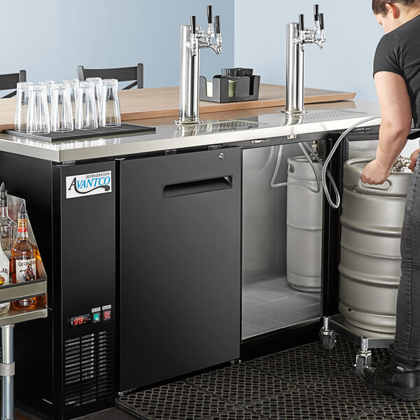 A woman pouring beer from a keg using an Avantco Black Kegerator with triple taps.