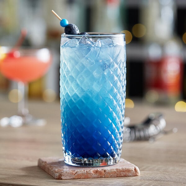 A close-up of a blue Anchor Hocking cooler drink on a table with a blue straw.