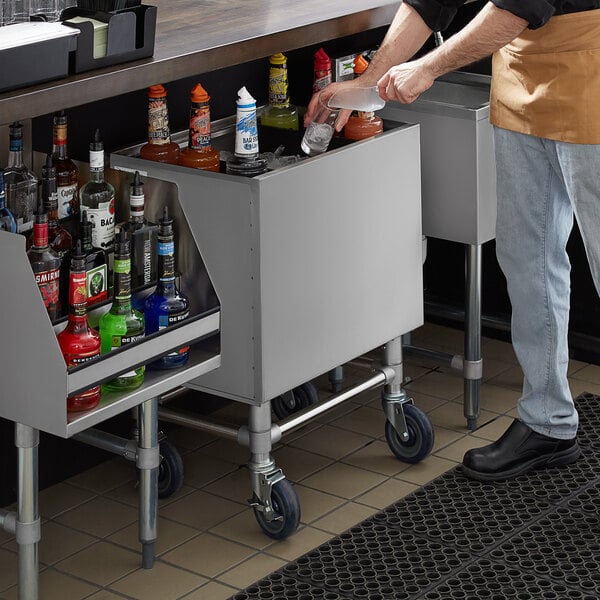 A man standing behind a Regency stainless steel portable ice bin on a counter in a cocktail bar.