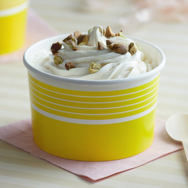A yellow Choice paper cup filled with white frozen yogurt topped with whipped cream and nuts.