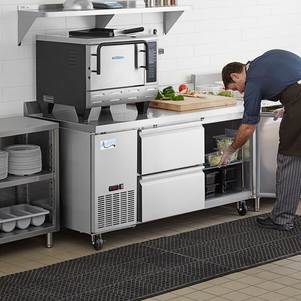 A man using an Avantco stainless steel worktop refrigerator in a professional kitchen.
