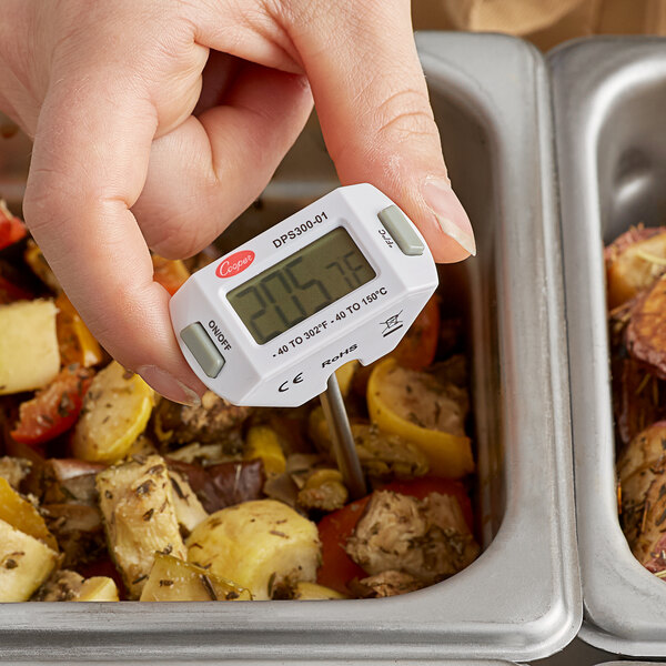 A hand using a Cooper-Atkins digital pocket probe thermometer to check the temperature of food in a container.