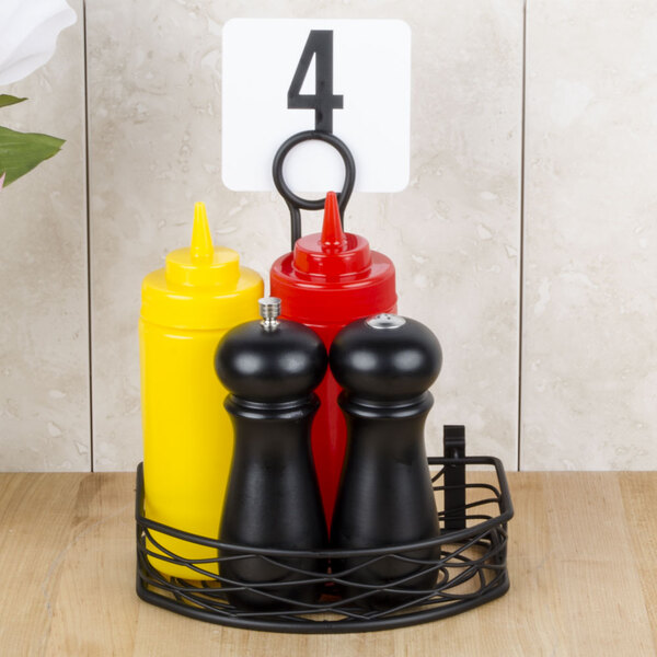 A black American Metalcraft wrought iron condiment caddy holding three condiments and a pepper mill.