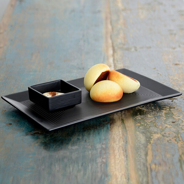 A Front of the House Spiral Ink semi-matte black rectangular porcelain plate with food on it.