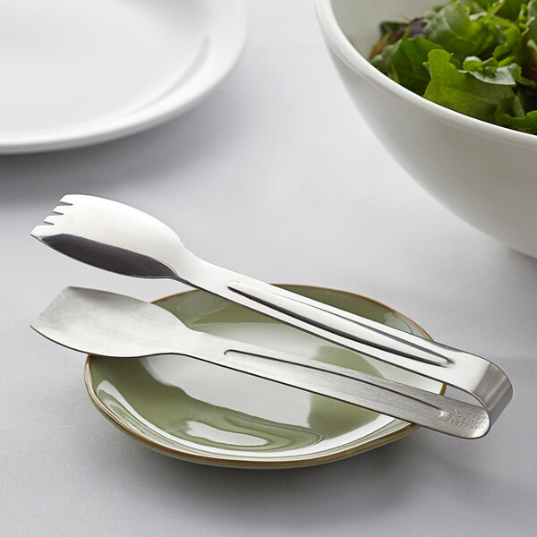 A white plate with a bowl of salad and Carlisle stainless steel salad tongs.
