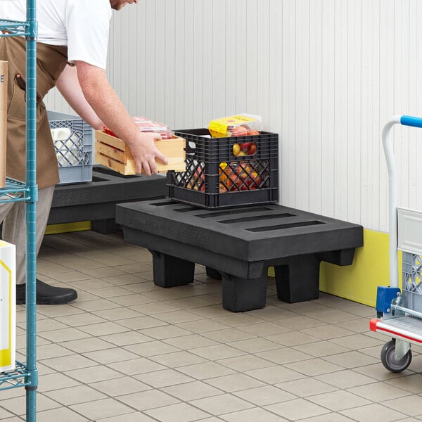 A man holding a black plastic dunnage rack with grey crates on top.