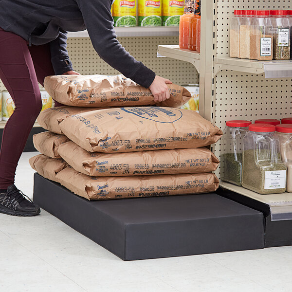 A woman places a brown bag on a stack of bags on a grey table.