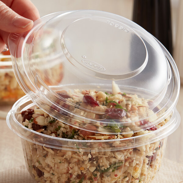 A person's finger placing a Dart plastic dome lid on a plastic container with food inside.