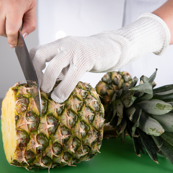 A person wearing a San Jamar D-Shield cut-resistant glove cutting a pineapple.