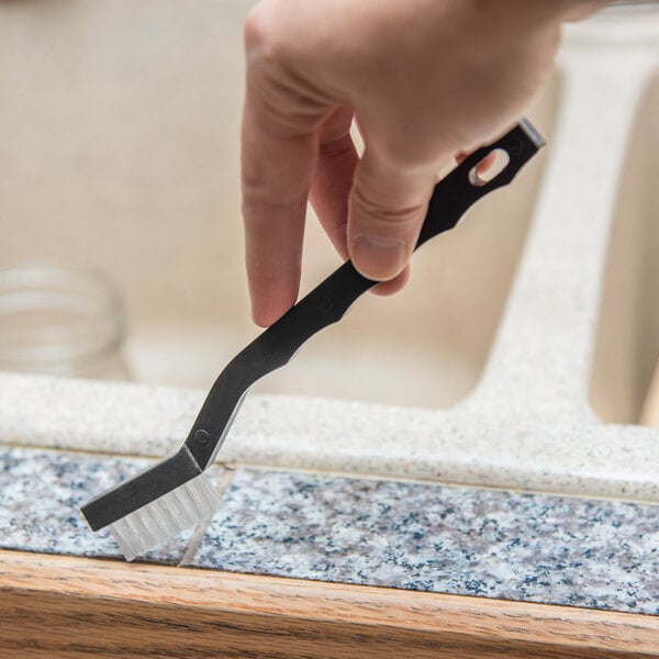 A hand holding a Carlisle nylon utility brush with a black handle brushing a kitchen counter.