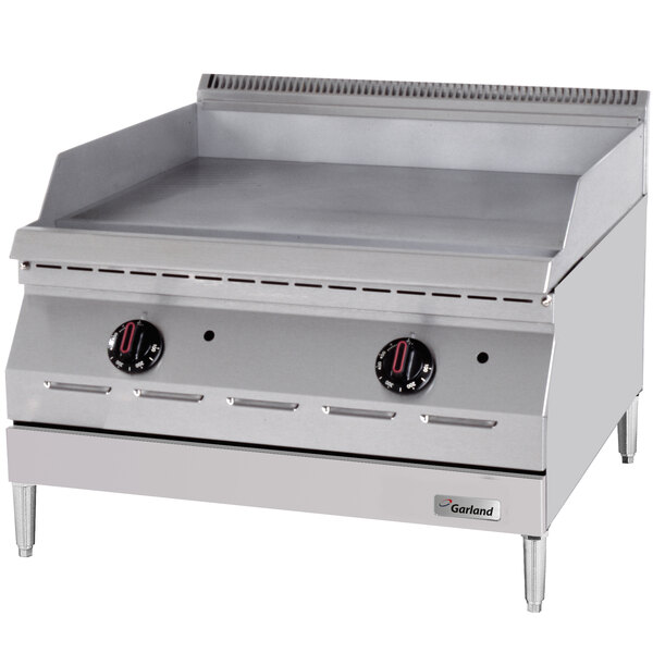 A large steel Garland countertop griddle with two black and red thermostatic controls.