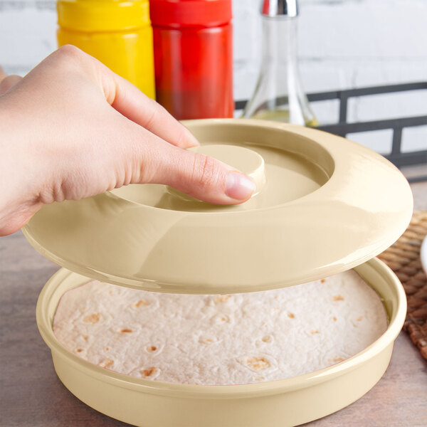 A person holding a Thunder Group Nustone tan melamine lid over a tortilla in a round container.