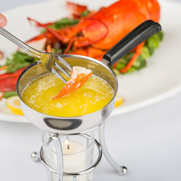 The handle of a Vollrath butter pan with a fork in it over a pot of melted butter with a lobster on the fork.