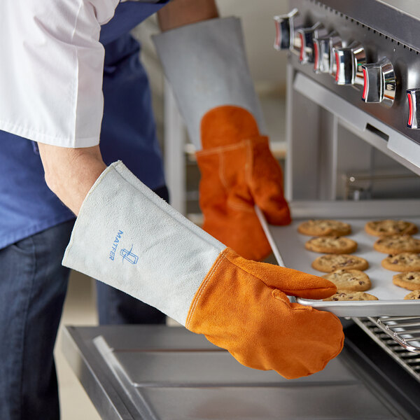 A person wearing Matfer Bourgeat orange leather oven mitts puts cookies in the oven.