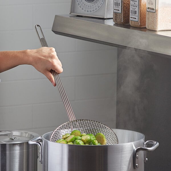 A hand using a Carlisle round mesh skimmer to stir food in a pot.