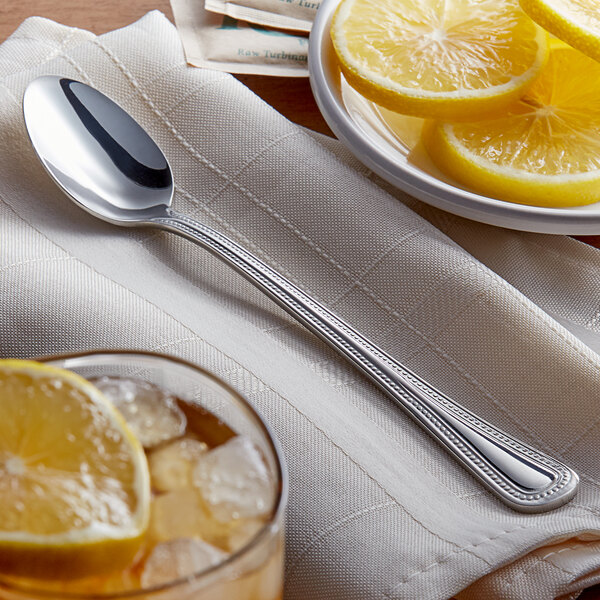 An Acopa stainless steel iced tea spoon with a lemon slice on it on a table with a bowl of lemons.