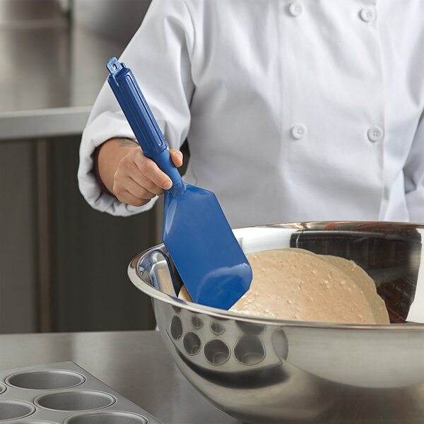 A person in a chef's uniform mixing dough in a bowl with a blue Carlisle Sparta paddle.