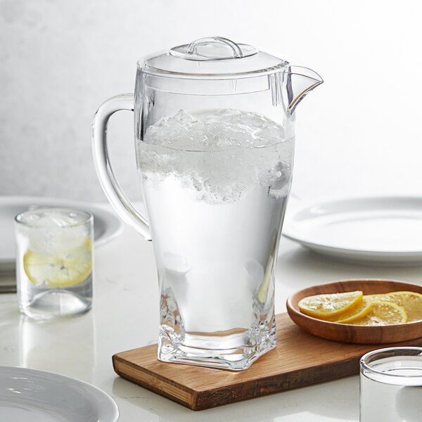 An Arcoroc SAN plastic pitcher of water with ice and a glass of lemons on a wooden board.
