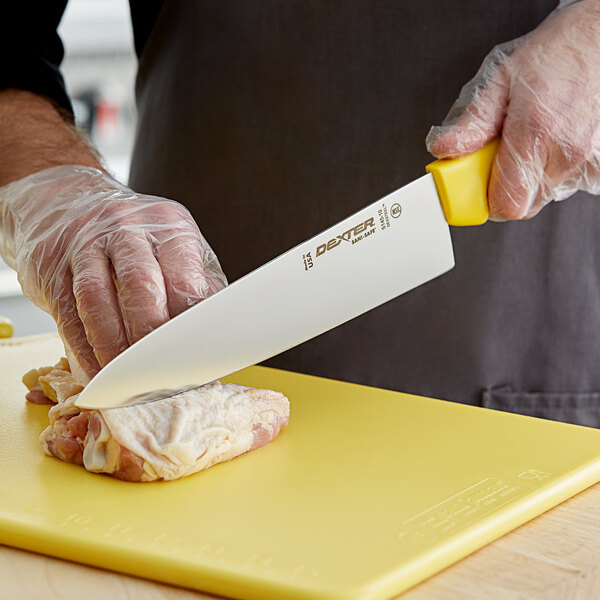 A person in gloves using a Dexter-Russell yellow chef knife to cut meat on a yellow cutting board.