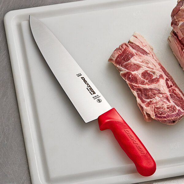 A Dexter-Russell red chef knife on a cutting board next to a piece of meat.